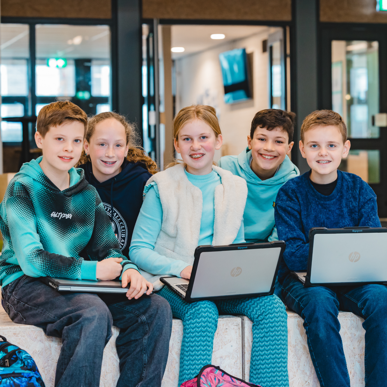5 leerlingen zittend op een blok, 2 daarvan zitten wat achter de voorste drie. Drie leerlingen hebben hun laptop open geklapt op schoot, een leerling heeft deze dicht op schoot ligge.