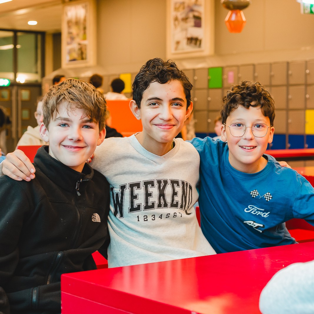 3 jongens in aula T-gebouw, middelste jongen slaat arm om buitenste twee jongens
